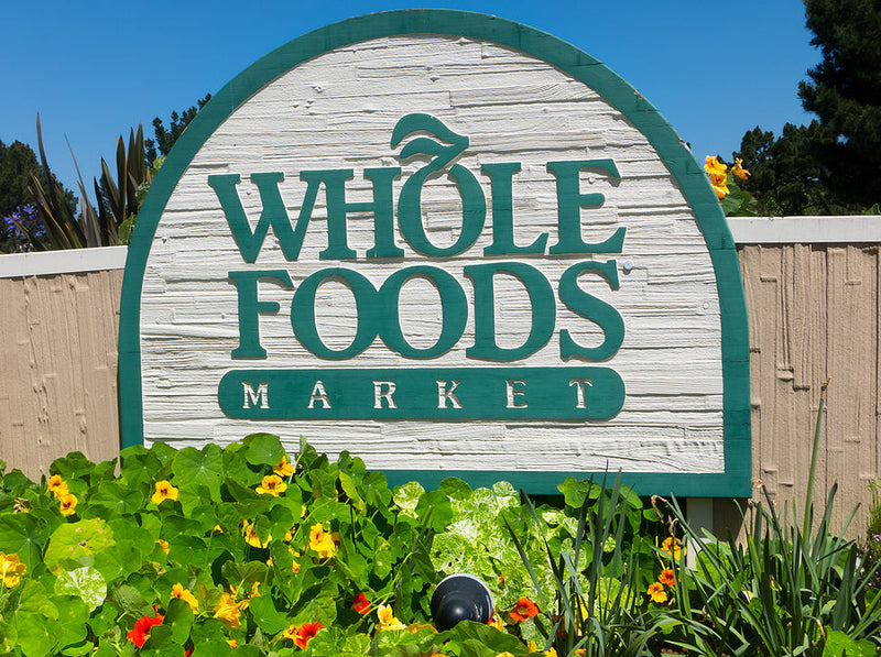 Wooden Whole Foods Market sign surrounded by greenery and flowers.