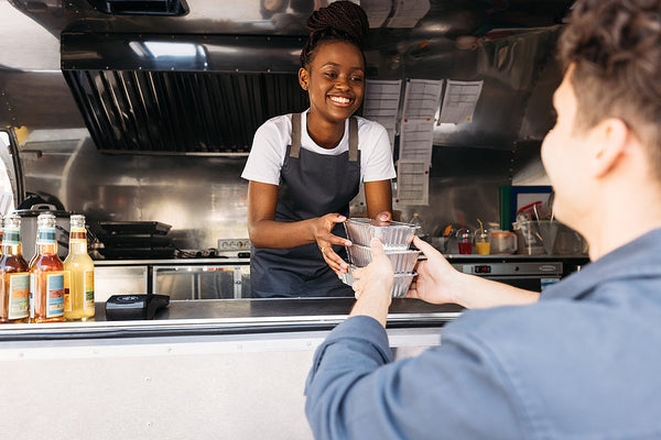 Smiling food truck chef handing meal to customer at service window