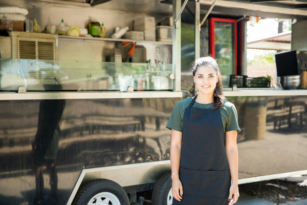 A food truck owner standing beside a mobile kitchen, ready to serve customers outdoors.