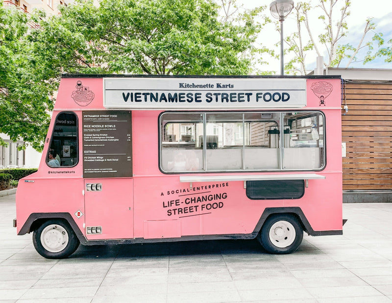 A pink Vietnamese street food truck parked outdoors, representing a modern entrepreneurial venture.