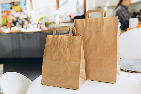 Brown paper bags ready for food delivery on a table in a ghost kitchen setup.
