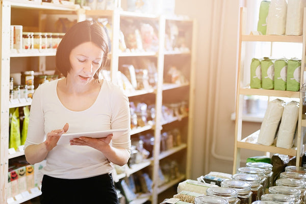 Smiling food entrepreneur holding a tablet in a grocery-style commercial kitchen