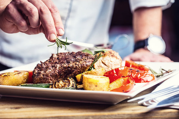 Chef plating a gourmet dish with roasted vegetables and fresh herbs in a commercial kitchen setting