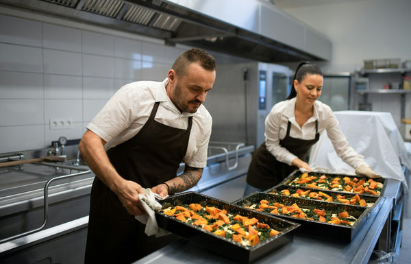 Chefs working in a large industrial kitchen preparing multiple trays for catering or delivery