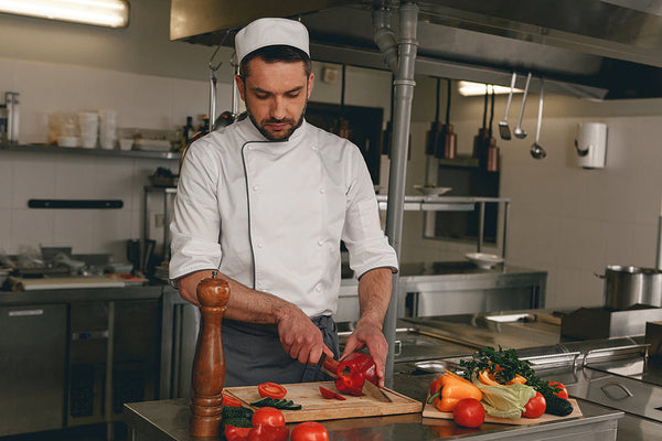 Professional chef slicing red pepper in a fully equipped commercial kitchen space.