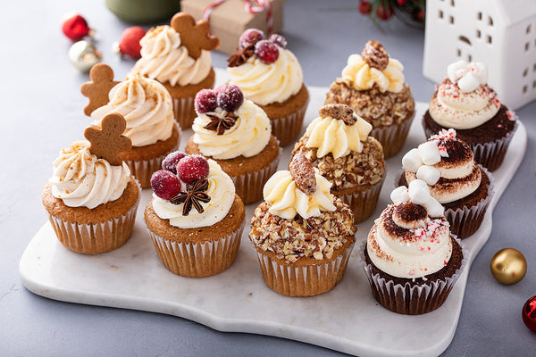 A festive tray of assorted holiday cupcakes displayed on a marble board, highlighting seasonal baked goods prepared in a shared kitchen.