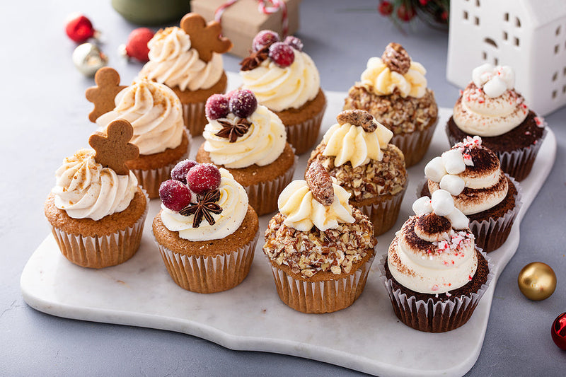 A festive tray of assorted holiday cupcakes displayed on a marble board, highlighting seasonal baked goods prepared in a shared kitchen.