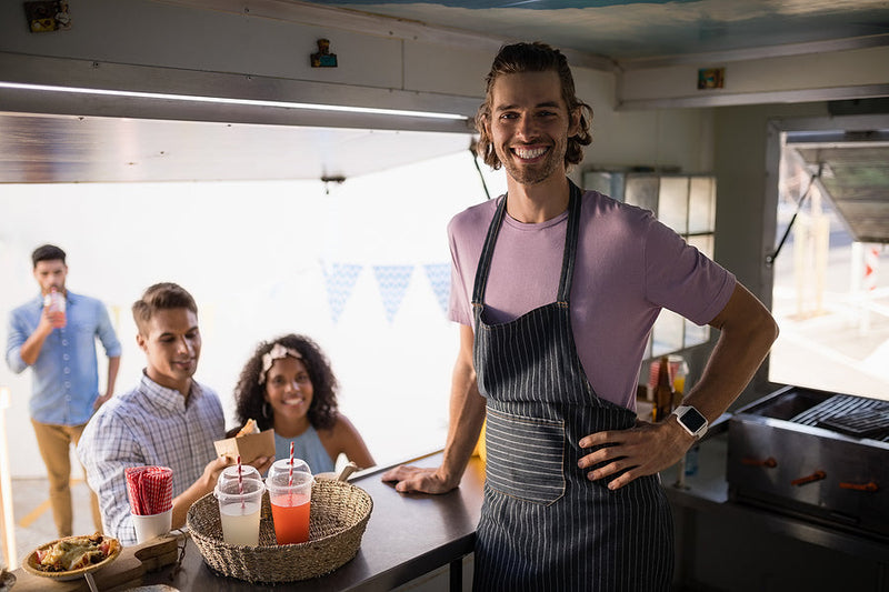 Smiling food truck owner serving customers with colorful drinks and snacks on the counter